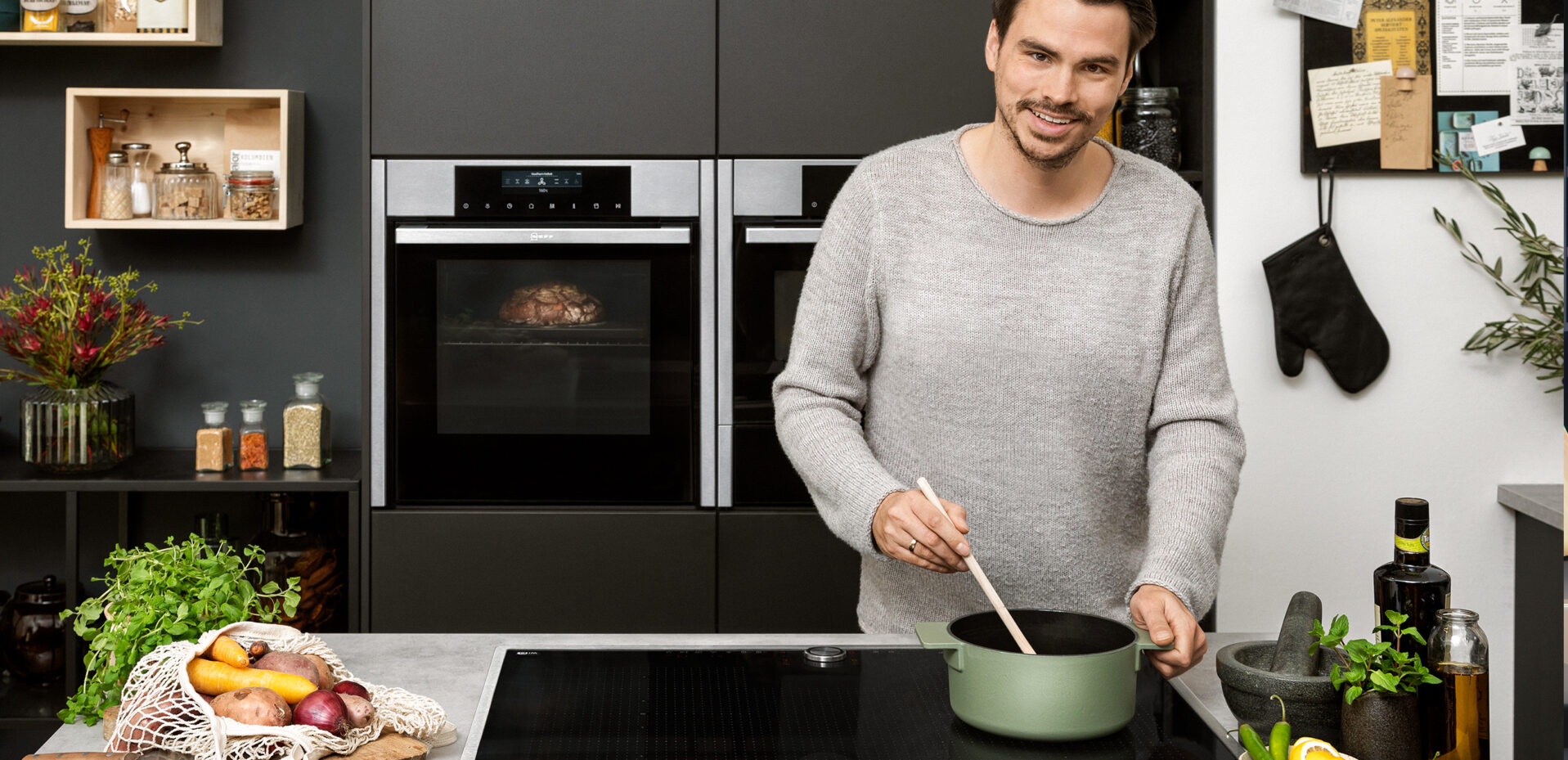 Mann steht hinter Kücheninsel und kocht in einem Topf